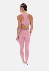 Rózsaszín sportos crop top és leggings elasztikus anyagból, széles derékpánttal, amelyen "TED BAKER SPORT" felirat található. Fehér tornacipők.