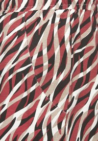 Geprinte stof met gedurfde, golvende strepen in rood, bruin, beige en wit. Heeft een zijzak met zichtbare stikseldetails.