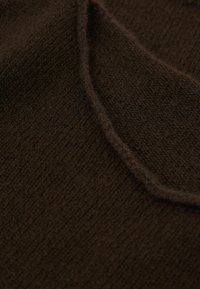 Dunkelbrauner, strukturierter Strickstoff mit feinem Rippenmuster und einer gebogenen Kantennaht. Weiches, warmes Materialaussehen.