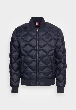 Tmavě modrá prošívaná bunda ve stylu bomber, vybavená předním zipem a žebrovanými manžetami. Malé logo na hrudi a kontrastní podšívka.