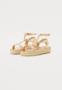 Sandales en métal doré avec une plateforme en jute tressé, dotées de plusieurs brides de cheville et d'une semelle intérieure lisse.