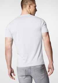 Biała koszulka z krótkim rękawem, wykonana z miękkiej bawełny, z okrągłym dekoltem. Z tyłu znajduje się subtelne logo marki, w połączeniu z dopasowanymi szarymi dżinsami.