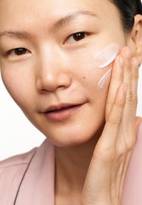 Idratante per il viso applicato sulla pelle. Texture in gel trasparente con una finitura liscia. Il modello ha la pelle chiara e indossa una maglia rosa chiaro.