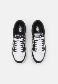 Baskets de sport noires et blanches avec un bout perforé, des accents contrastants, un col rembourré et des lacets blancs. Logo de la marque sur la languette et sur le côté.
