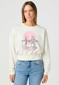 Suéter recortado crema con un gráfico rosa que presenta dos figuras contra un fondo circular rosa. Puños y dobladillo acanalados.