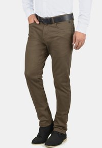 Pantalones de mezcla de algodón en verde oliva con un corte ajustado. Presenta una cinturilla estándar, pasadores para cinturón y bolsillos laterales. Combinados con zapatos negros.