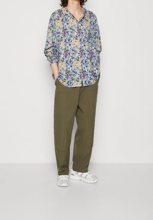 Kleurvol longsleeve shirt met bloemenprint in tinten paars en beige, gecombineerd met ruime olijfgroene broek en witte sneakers.