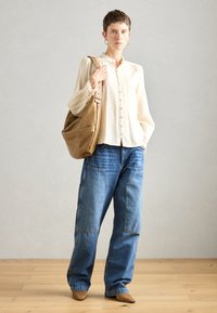Camicia beige con bottoni e dettagli in pizzo, abbinata a jeans in denim blu larghi e stivali alla caviglia in pelle color nocciola. Borsa marrone a tracolla.