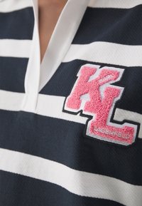 Camisa polo a rayas en azul marino y blanco con un escote en V profundo. Presenta un logotipo en aplicación texturizada en rosa y negro "KL" con "LAGERFELD" debajo.