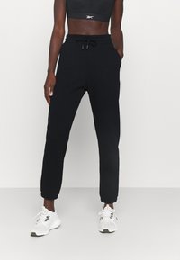 Svarta joggerbyxor med elastisk midja och dragsko, med sidofickor och avsmalnade mudd. Bärs med vita träningsskor.