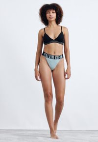 Zwarte beha met dunne bandjes, gecombineerd met lichtblauwe hoog uitgesneden slipjes met een zwarte Calvin Klein logo tailleband.