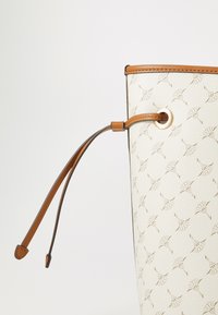 Sac seau blanc avec un motif en relief subtil et des accents en cuir tan, y compris une fermeture à cordon et un œillet décoratif en or.