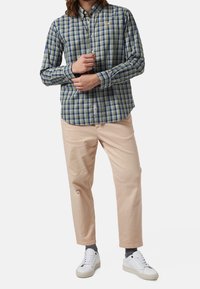 Camisa de cuadros verde y azul con botones y mangas largas, combinada con chinos color beige claro y zapatillas blancas. Tejido suave, corte ajustado.