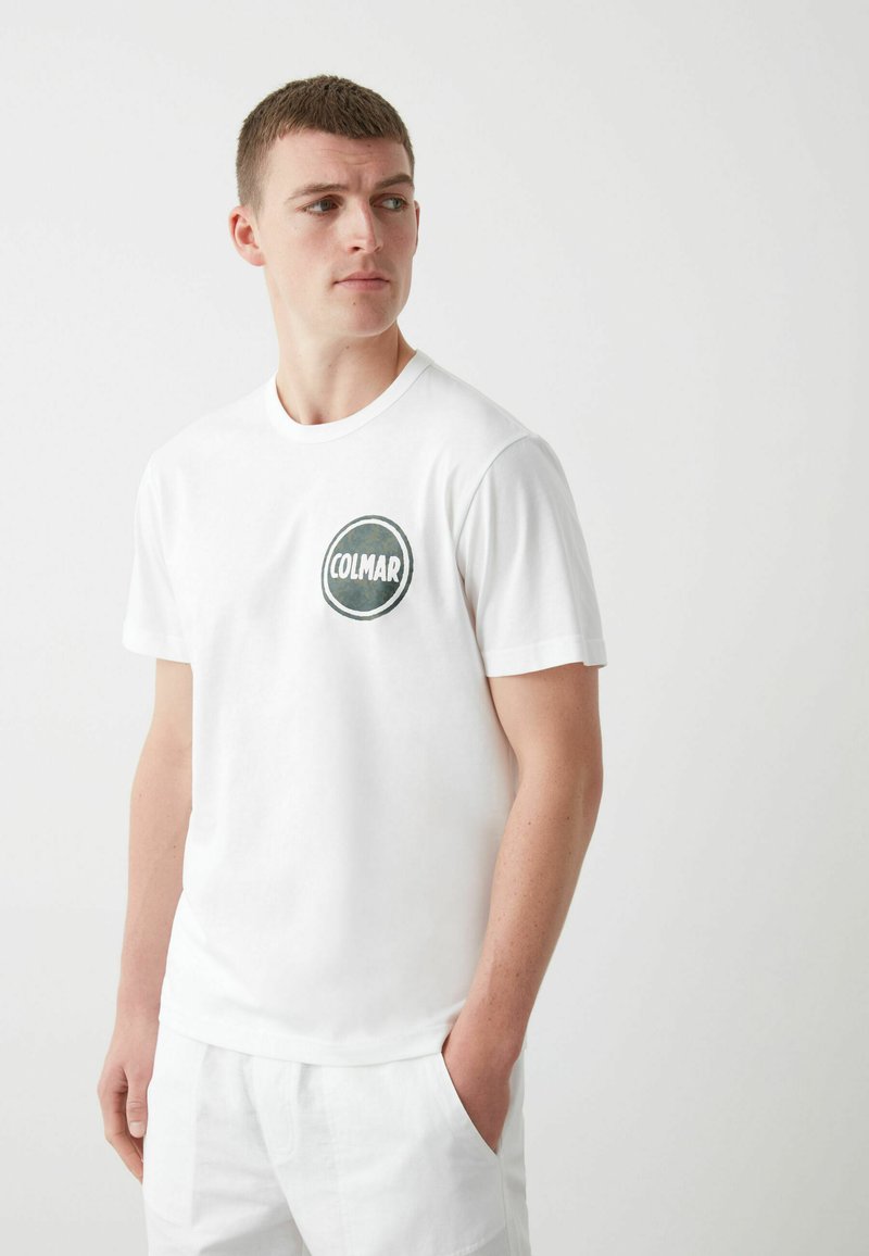 Camiseta de algodón blanca con un logo redondo en azul marino y verde que dice "COLMAR" en el lado izquierdo del pecho. Cuello redondo y mangas cortas.