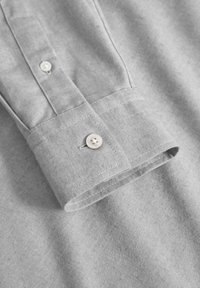 Camisa de botones de color gris claro con un cuello estructurado y un botón único en el puño, con un sutil tejido texturizado.