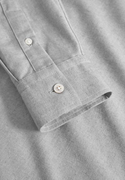 Chemise boutonnée gris clair avec un col structuré et un unique bouton au poignet, présentant un tissage texturé subtil.