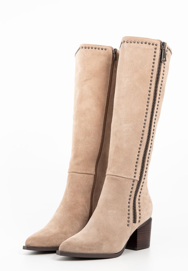 Botas altas de ante en color beige, con punta afilada, cremalleras laterales y acentos con tachuelas a lo largo de las costuras. Tacón de madera apilada.