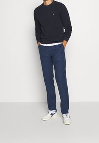 Merinovillaneule, jossa on pyöreä kaula-aukko, yhdistettynä vaaleansinisiin pellavahousuihin. Valkoiset lenkkarit, joissa on tummansinihköjä yksityiskohtia. Yksinkertainen muotoilu, ilman näkyviä kuvioita.