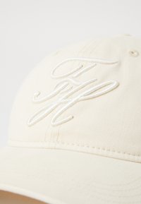 Cappello beige in cotone con iniziali ricamate bianche. Dotato di visiera curvata e dettagli cuciti sulla corona. Design semplice e pulito.