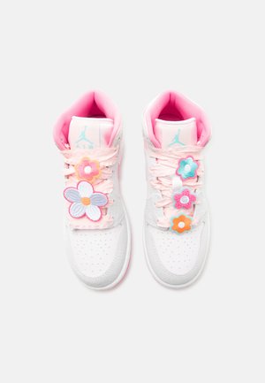 Ζευγάρι λευκών και ροζ αθλητικών παπουτσιών Air Jordan με διακοσμητικά λουλούδια σε παστέλ χρώματα προσαρτημένα στα κορδόνια, σε θέα από πάνω.