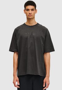 Mørkegrå oversized T-shirt lavet af blødt stof, med korte raglanærmer og diskrete prægede logo detaljer på forsiden.