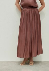 Gonna maxi in tessuto rosa polveroso, caratterizzata da un design plissè, una vita elastica e abbinata a sandali gialli con cinturini.