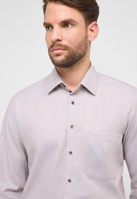Lichtpaarse shirt met lange mouwen en een gestructureerd patroon, knoopsluiting aan de voorkant, een enkele borstzak en contrasterende knoopdetails.
