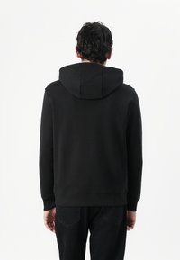 Sort hætte sweatshirt lavet af blødt stof med et simpelt design, der har ribbet kant og manchetter, vist fra ryggen.