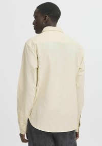 Vaaleankeltainen pitkähiha shirt, jossa on viisto kaulus, napitettavat hihansuut ja suora helma. Kangas näyttää teksturoidulta ja siinä on rento istuvuus.