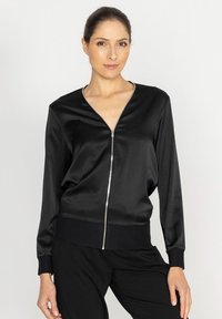 Czarna satynowa kurtka bomberka z zamkiem z przodu, dekoltem w serek i ściągaczami na rękawach. Miękka w dotyku i luźnego kroju, idealna na co dzień.