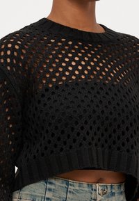 Maglione corto nero lavorato a maglia con un design a rete, scollo e orlo a coste. Caratterizzato da un motivo a trama aperta e da una finitura testurizzata.