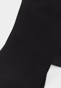 Κοντινό πλάνο μαύρου υφάσματος με ορατές ραφές και διακριτική υφή σε μια λεία, καμπυλωτή επιφάνεια.