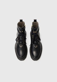 Bottes noires en cuir à la cheville avec un bout arrondi, des accents en métal doré, un laçage à l'avant et un col rembourré pour plus de confort.