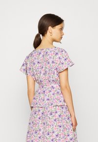 Top peplum floral com flores roxas e cor-de-rosa sobre um fundo claro. Mangas curtas, gola redonda e cintura ajustada.