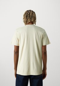 Camiseta de manga corta verde claro, con cuello redondo, textura de algodón suave, corte relajado, costuras visibles en el dobladillo, combinada con jeans oscuros.