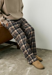 Beige plaid trousers with navy and brown accents, featuring a loose fit and side pockets, paired with tan slip-on footwear.
