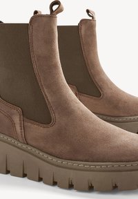 Brown suede ankle boots with elastic side panels and a thick, textured rubber sole. Features stitch detailing and pull tabs on the heel.