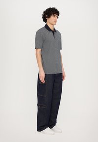 Kortermet polo i marineblått og hvit geometrisk mønster med mørk krage, paret med mørke denim cargo-bukser og hvite sneakers.