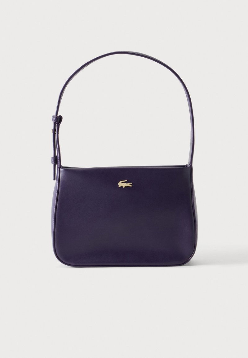 Petit sac à épaule en cuir violet foncé avec une fine bandoulière réglable et un petit logo crocodile doré au centre à l'avant.