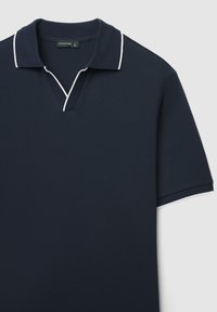 Polo blu navy con maniche corte, tessuto strutturato, collo a V e cuciture bianche a contrasto lungo il bordo del collo e delle maniche.