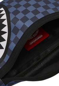 Funda con cremallera a cuadros azul y negro con un diseño de tiburón; textura suave; etiqueta roja visible en el interior; forro negro.