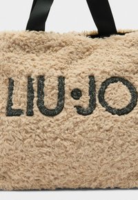 Borsa in pelliccia testurizzata beige con lettering nero "LIU•JO", dotata di manici in tessuto nero per il trasporto. Il design è morbido e soffice.