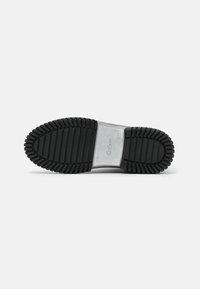 Suela de zapato de goma negra con surcos profundos, sección central plateada, y el nombre de la marca "Gabor" grabado en el centro.
