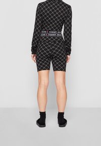 Set di abbigliamento attivo nero con motivo geometrico, maniche lunghe e pantaloni corti abbinati a vita alta. Marchio visibile sulla banda in vita.