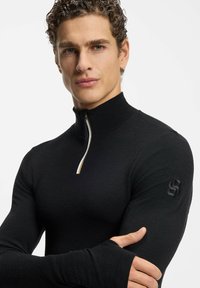 Czarna koszula z długim rękawem, z wysokim kołnierzem i zamkiem na pół długości; wykonana z fakturowanej tkaniny, z logo na lewym rękawie.