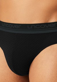 Black patterned brief featuring a textured fabric with a diamond pattern, elastic waistband with "uncover" branding in gray.