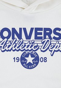 Λευκό φούτερ με κουκούλα με μπλε τυπωμένο κείμενο, "CONVERSE Athletic Dept." με ένα κυκλικό λογότυπο, "Chuck Taylor All Star" και το έτος "1908."