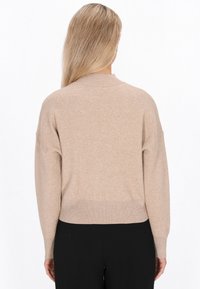 Beige gestrickter Pullover mit rundem Ausschnitt, überschnittenen Schultern und geripptem Saum. Weiche Textur, lockere Passform und lange Ärmel.