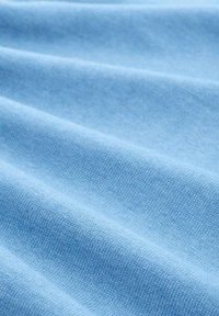 Weiches, hellblaues Strickgewebe mit sichtbarer feiner Textur und sanften Falten, die geschmeidige, fließende Linien erzeugen.