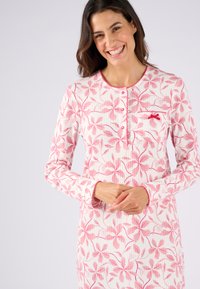 Vestido de noche de manga larga en blanco con estampado floral rosa, con botones en el frente y un pequeño bolsillo en el pecho con un acento de lazo. Textura de tela suave.